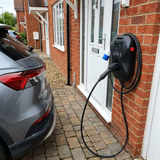 32A EV wall charger wall-mounted beside a front door, charging a grey electric car on a block paved driveway